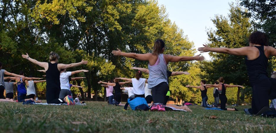 Group of adults practicing yoga outdoors in a park surrounded by trees.